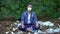 Female in protective mask sitting on plastic garbage in forest, toxic future