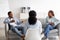 Female psychotherapist sitting with her back to camera during session with irritated black couple at clinic