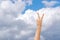 Female raised hand showing two fingers gesture in the air with clouds and sky on background.