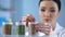 Female researcher putting sticker on bottle with seeds, pesticide development