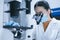 Female researcher using the inverted microscope to look at culture cells on a slide for bioassay of the drug