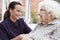 Female Resident Sitting In Chair And Talking With Carer In Retirement Home