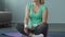 Female retiree sitting on fitness mat and warming up by stretching arms, workout