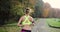 Female runner in the park. Woman in colorful jogging suit listens to the music and runs along the path in the park