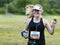 Female runner smilines and gives hang loose sign while racing in a park