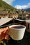 Female`s Hand Holding a Cup of Hot Coffee against Blurry Caucasus Mountains and Mestia Town in Background