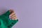 Female\\\'s hand with purple nails wearing green jacket on purple background