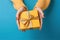 Female\\\'s hands in yellow and light blue, cyan tone, holding a gift box on yellow pastel background. Christmas and Valentine\\\'s Da