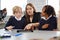 Female school teacher helping two kids using a tablet computer at desk in a primary school classroom, front view