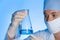 Female scientist holding test flask with sample on color background.