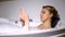 Female scrolling social media, lying in bathtub with foam bubbles, relaxation