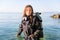 Female Scuba Diving Instructor Standing in Water Wearing a Dry Suit, a Twin Tank and Holding Fins