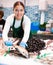 Female seller in apron shows hands fish trout on counter in supermarket