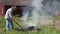 Female senior gardener burn grass and refuse in fire on meadow in rural village house yard. 4K