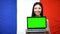 Female showing laptop with green screen against French flag background, study