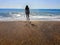 Female silhouette goes in the sea water on a gravel-sand beach. Young adult girl on the beach - beautiful background with copy