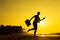 Female Silhouette staying along Ocean Coast with Luggage Bag enjoying scenic View Sea and Sunrise on background. Beach Holiday Co