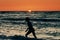 Female silhouette walking in sea waves at summer sunset, half sun below horizon, beachfront holiday