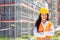 Female site supervisor wearing safety vest and helmet stands confidently in front of the construction covered in scaffolding