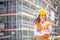 Female site supervisor wearing safety vest and helmet stands confidently in front of the construction covered in scaffolding