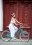 Female sits on bicycle against on background old red door