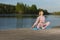 Female Sport Concepts. Relaxing Senior Woman in Sport Outfit Practicing Yoga On Wooden Stage Near Water With Closed Eyes Outdoor