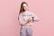 Female student checks time on wristwatch as hurries for classes, wears domestic clothes, isolated over pink background. Beautiful