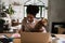 Female student studying at wooden desk being productive sitting with puppy working off laptop in modern kitchen.