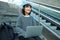 Female student works on project remotely, sits on stairs street, works on laptop, listens music in headphones and smiles