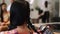 Female stylist applying hairspray fixing plaiting hairstyle on brunette hair back view slow motion. Hairdresser