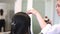 Female stylist hands applying hairspray fixing plaiting hairstyle on brunette hair back view slow motion. Hairdresser