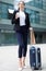 Female in suit with suitcase is drinking coffee
