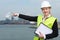 Female supervisor in hardhat and safety vest pointing to industrial site