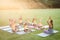 Female teacher and group of diverse students practicing yoga and meditating in the garden at school
