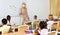 Female teacher in protective mask is giving lecture for primary school students in classroom