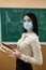 female teacher in protective mask near on green chalkboard