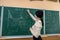 female teacher in protective mask near on green chalkboard