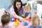 Female teacher sitting at table in playroom with three kindergarten children constructing