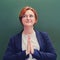 Female teacher stands with a beatific face and hands clasped in prayer. Holy schoolteacher with red hair