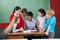 Female Teacher Teaching Schoolchildren At Desk