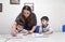 A female teacher teaching two little boys, explaining how to write in classroom at school