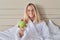 Female teenager with green apple in white bathrobe sitting in bed