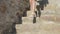 Female teenager legs in white sandals going on stony downstairs. Close up young girl in summer sandals walking down on