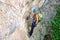 Female tourist with climbing gear and backpack resting on a via ferrata route, hanging from a locking carabiner