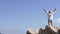 A female tourist raises her hands up standing on the edge of a cliff against the sky