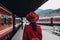 Female tourist in red hat and coat walking on platform waiting for passenger train arrival