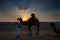 Female tourist taking picture of sunset while riding camel, Camelus dromedarius, at sand dunes of Thar desert, Rajasthan, India.