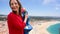 Female tourist using coin paid binoculars on high hill and looking at cityscape of Nazareth, Portugal