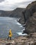 Female tourist in yellow raincoat black cliffs towering above the Atlantic ocean background