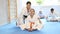 Female trainer helping woman in kimono sit in butterfly pose in sport gym
